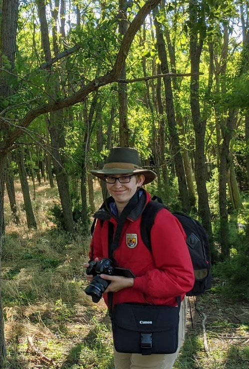 Nicole stands with her camera in a riparian woodland