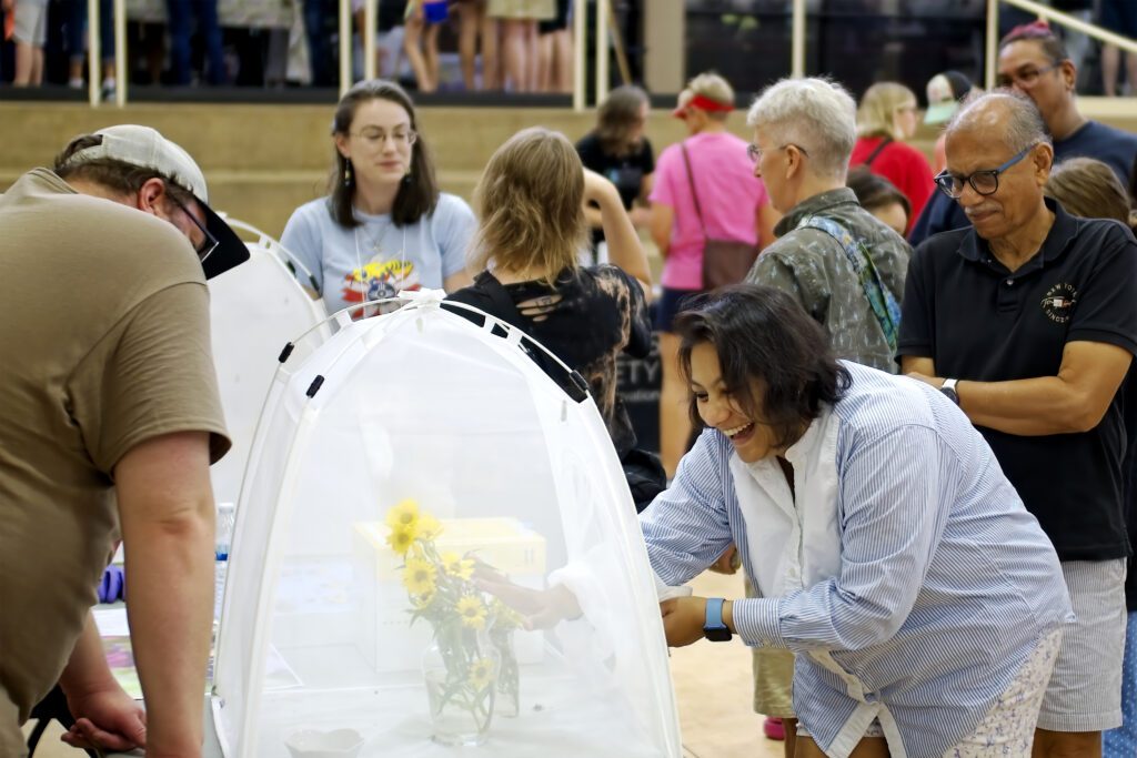 A visitor smiles in delight while petting a stinger-less bumblebee in a mesh bug dorm.