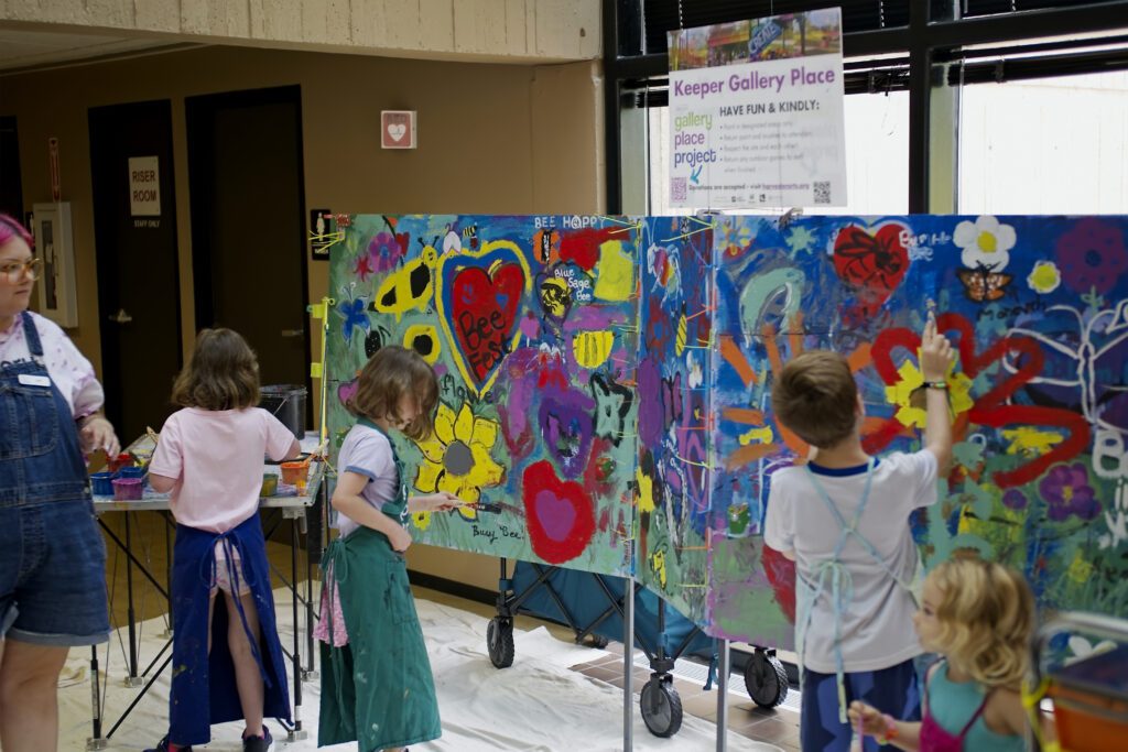 Kits in aprons paint colorful additions to a large mural of flowers, hearts, and bumblebees.