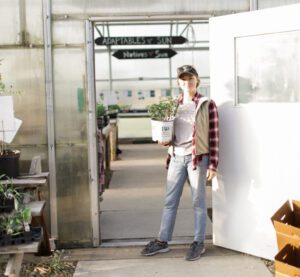 Katie Schmidt stands in the greenhouse carrying a plant.