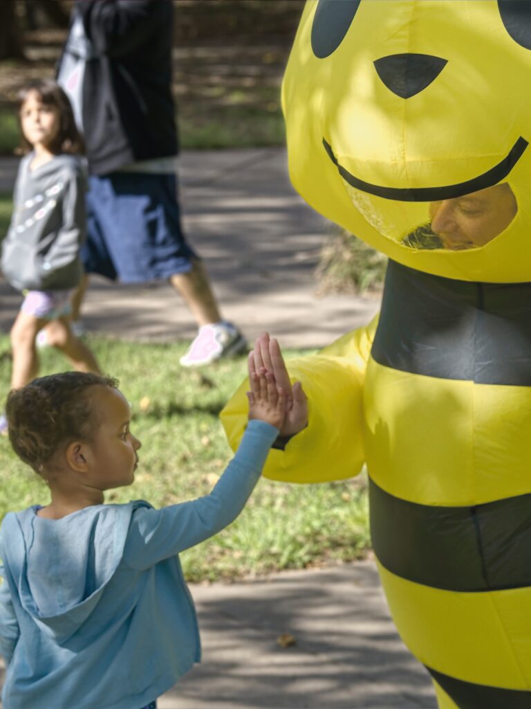 A bumblebee mascot gives a hi-five to a young child.