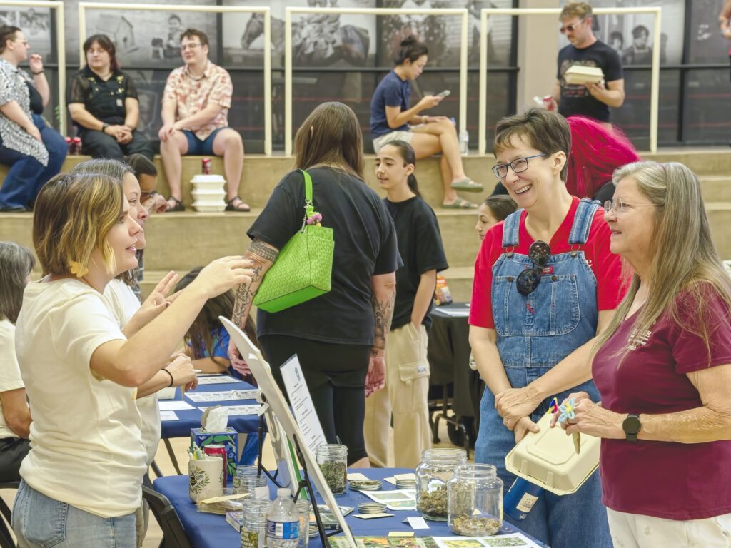 Volunteers and guests laugh as they gather around an informational table.