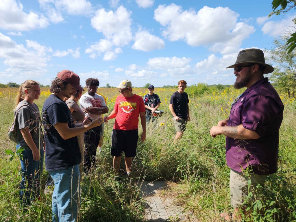 GG’s Grassland Ecology class at Friends University exploring Ninnescah with Dexter Mardis, Field Station Manager. One student holds a ringneck snake while others look on.
