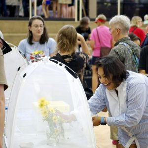 A visitor smiles in delight while petting a stinger-less bumblebee in a mesh bug dorm.