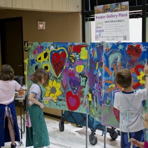 Kits in aprons paint colorful additions to a large mural of flowers, hearts, and bumblebees.
